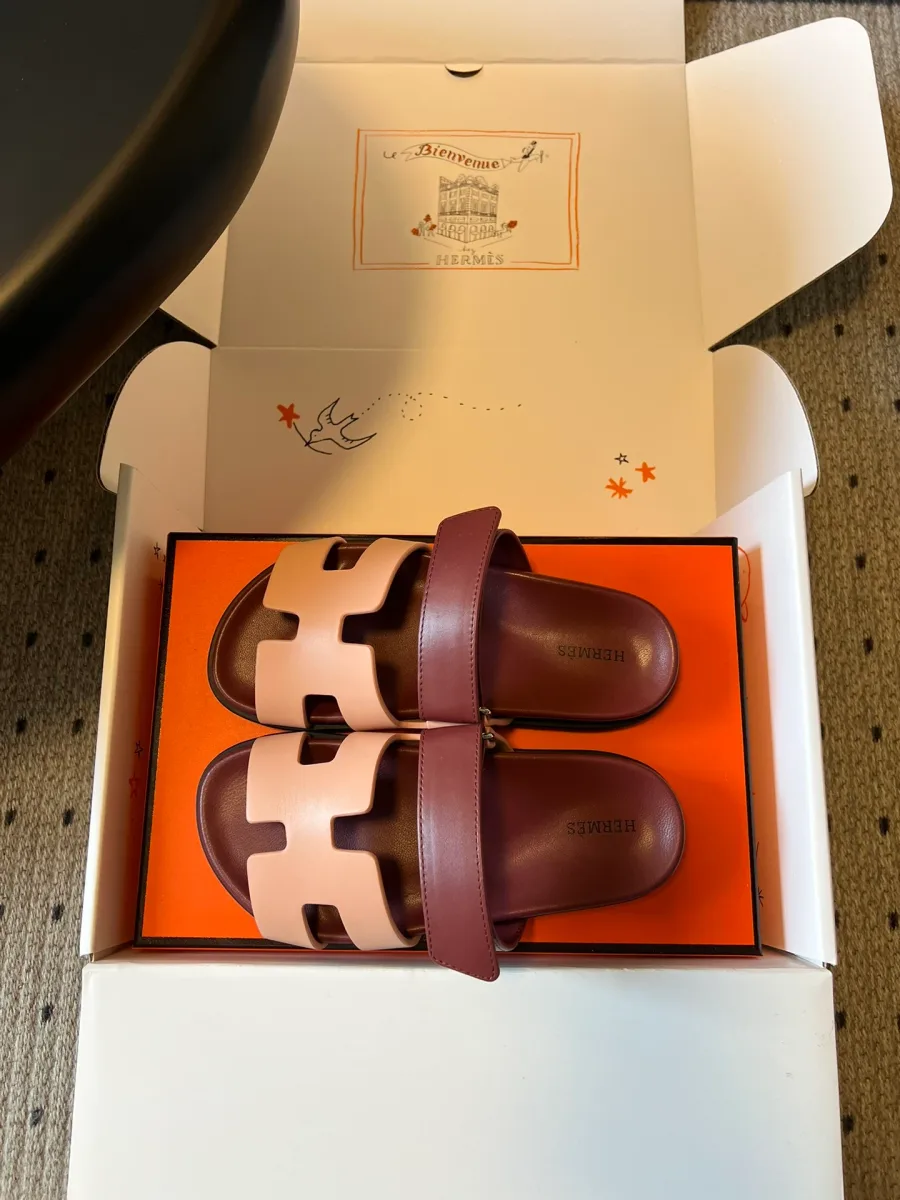 Пара бордово-розовых шлепанцев Hermes Chypre на коробке, вид сверху