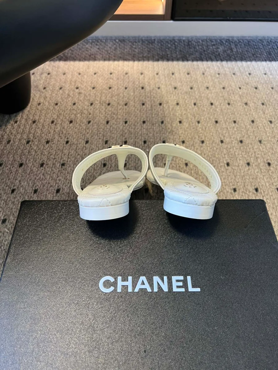 Задняя часть пары белых шлёпанцев на фирменной чёрной коробке Chanel
