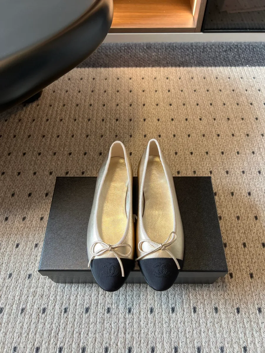 Золотистые балетки с контрастным чёрным мыском и бантиком, вид спереди на коробке