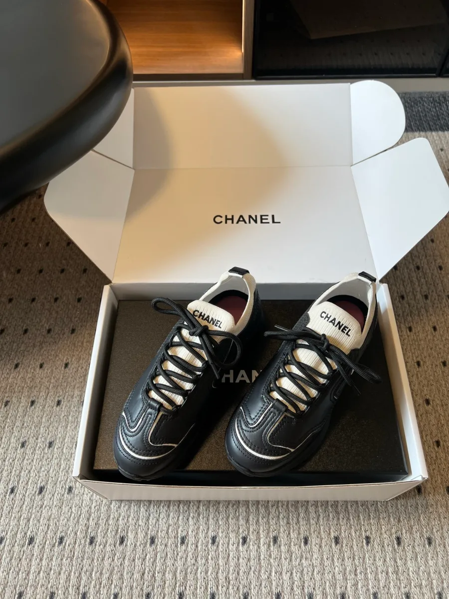 Пара чёрных кроссовок Chanel с белым кантом в открытой коробке, ракурс три четверти