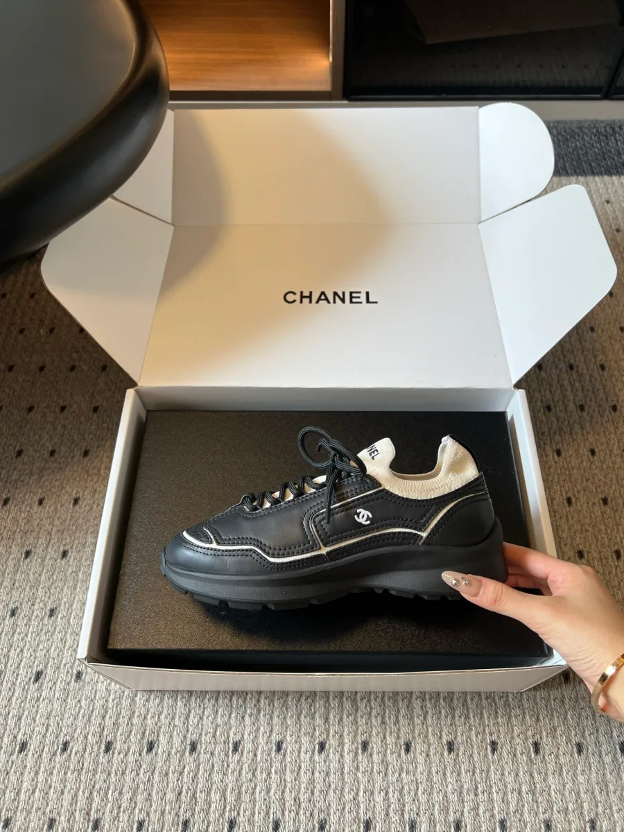 Чёрный кожаный кроссовок Chanel с белой строчкой, вид сбоку в руке