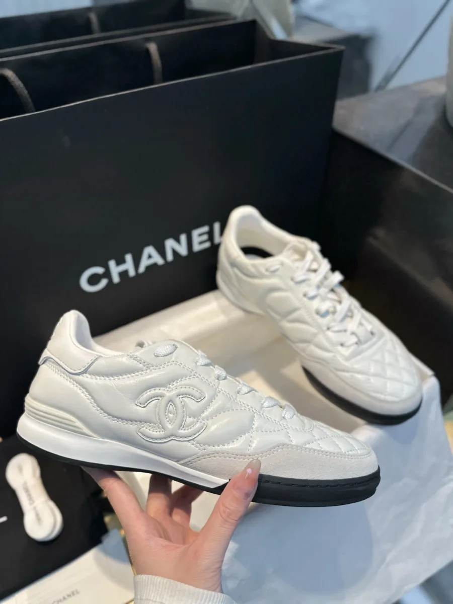Белый кожаный кроссовок Chanel с логотипом CC в руке, вид сбоку