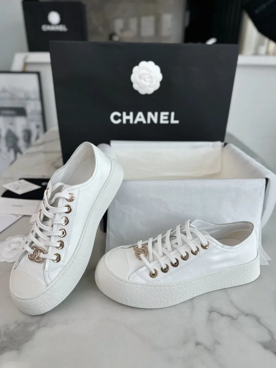 Пара белых кожаных кед Chanel в три четверти на фоне черного пакета