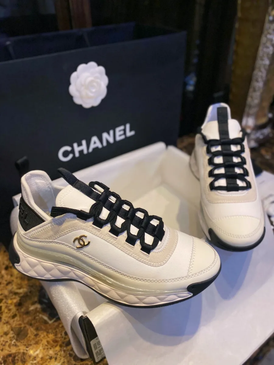 Пара массивных кроссовок Chanel в коробке на фоне пакета с камелией