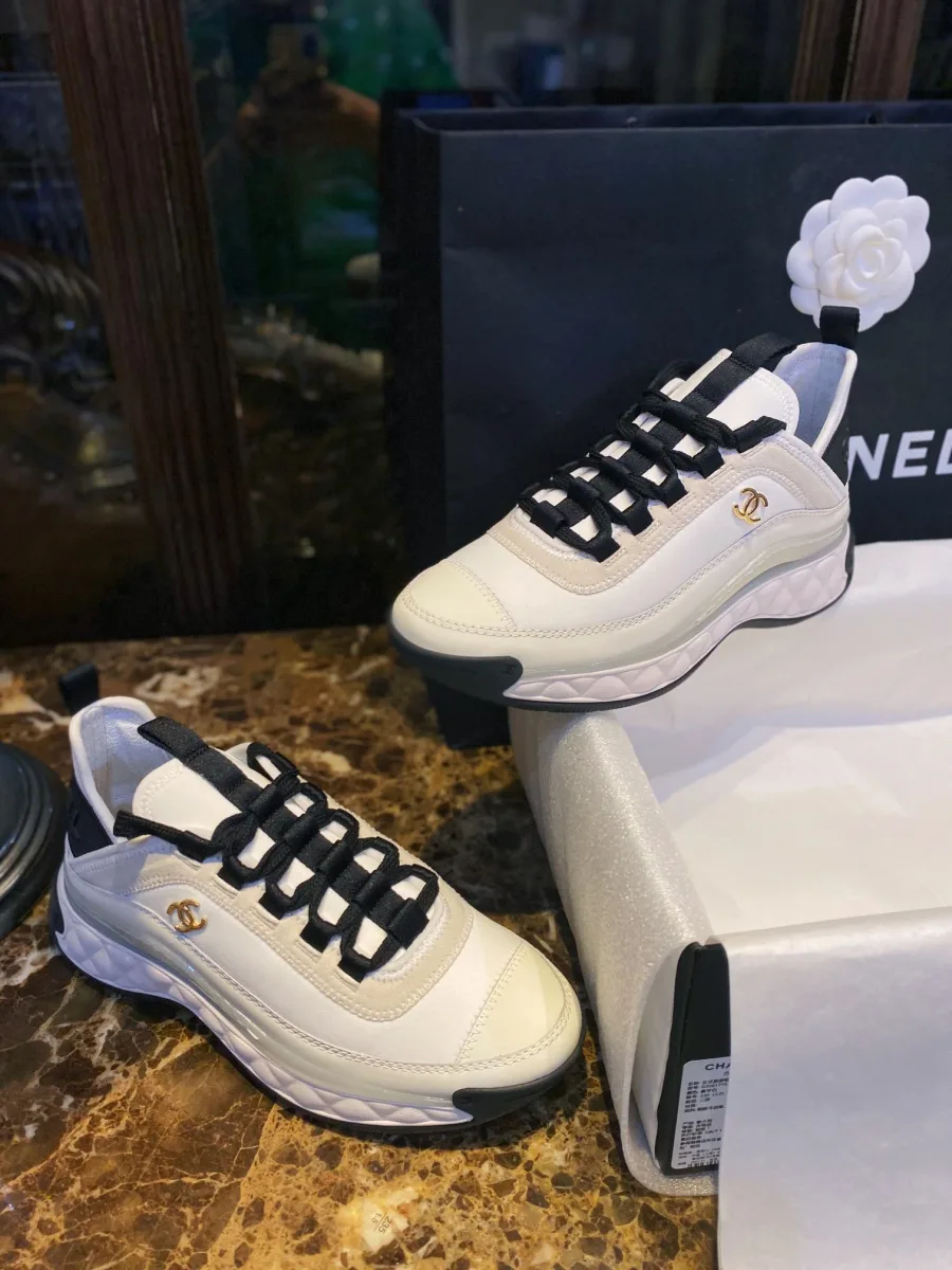 Бело-чёрные кроссовки Chanel в полупрофиль на фоне упаковки