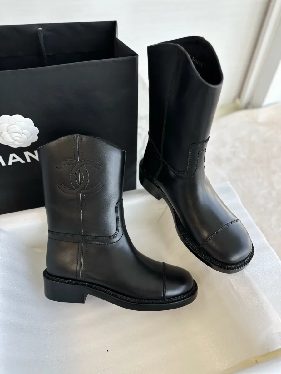 Пара чёрных сапог Chanel около фирменного пакета, боковой ракурс