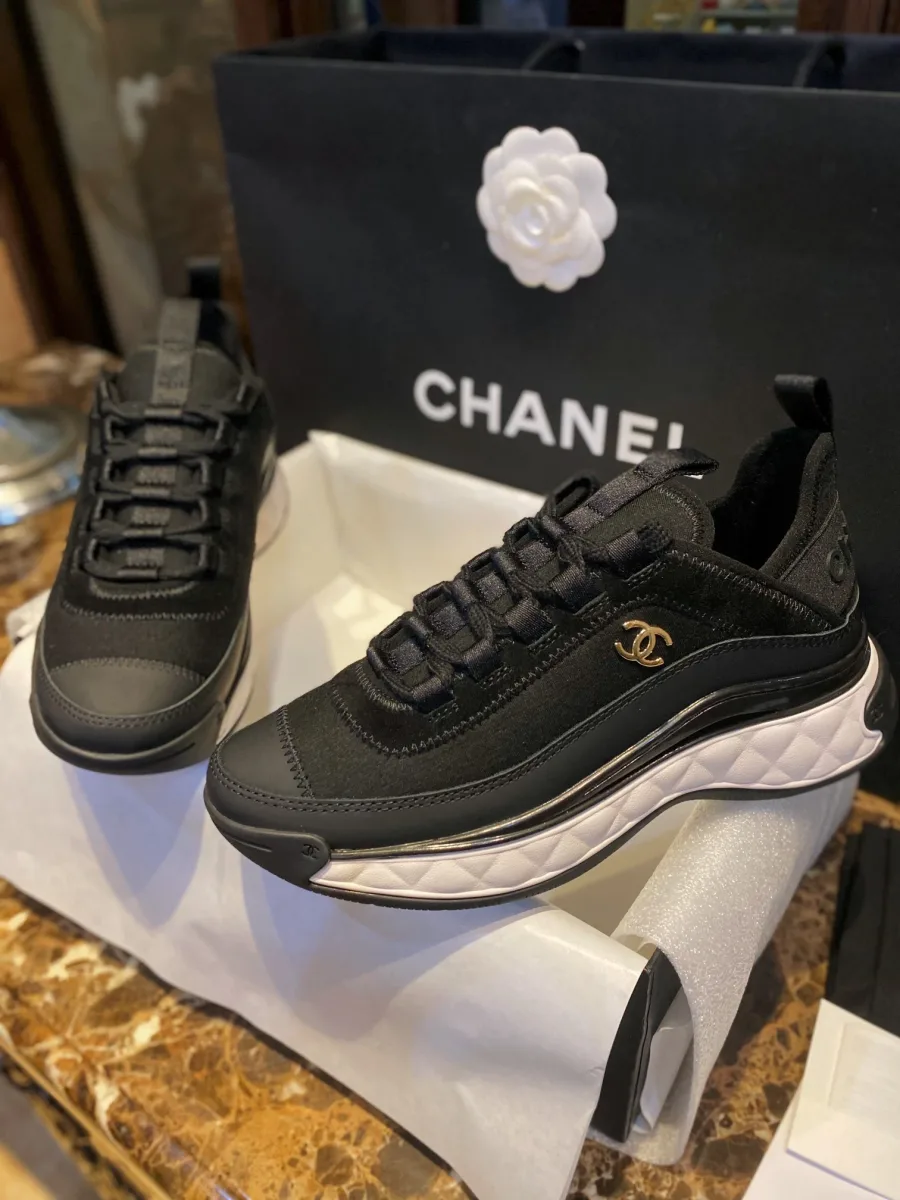Пара чёрных кроссовок в коробке на фоне фирменного пакета Chanel