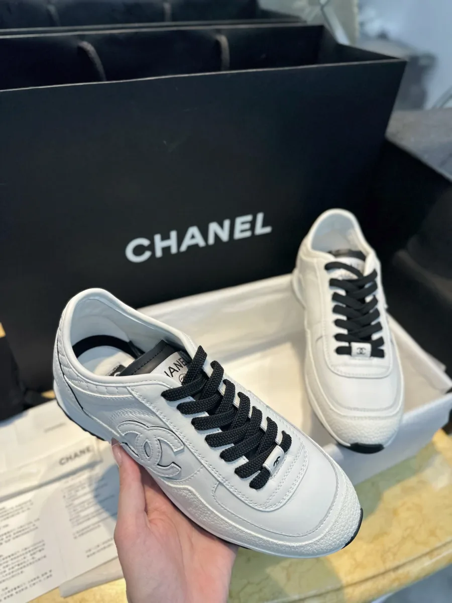 Белый кожаный кроссовок Chanel в руке, вид на боковой логотип CC
