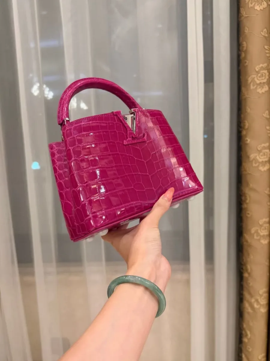 Компактная сумка Capucines BB из розовой кожи крокодила в руке, вид сбоку