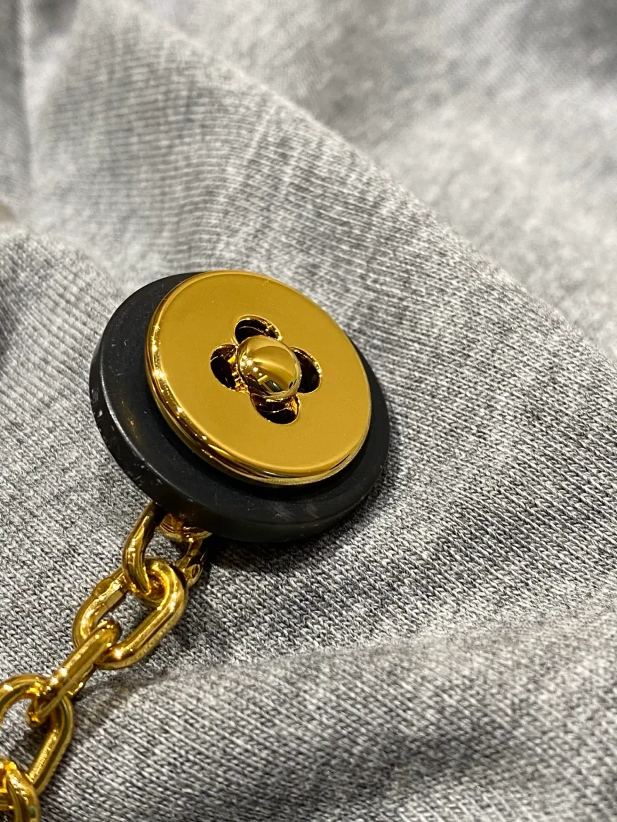 Макрофотография золотистой пуговицы с цветком Monogram и цепочки