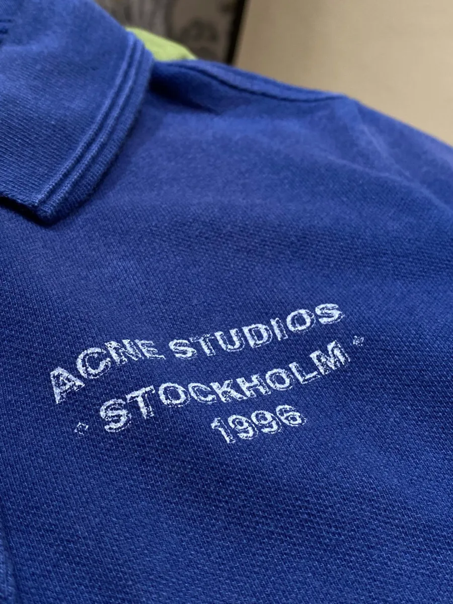 Крупный план белого принта Acne Studios Stockholm 1996 на синей ткани