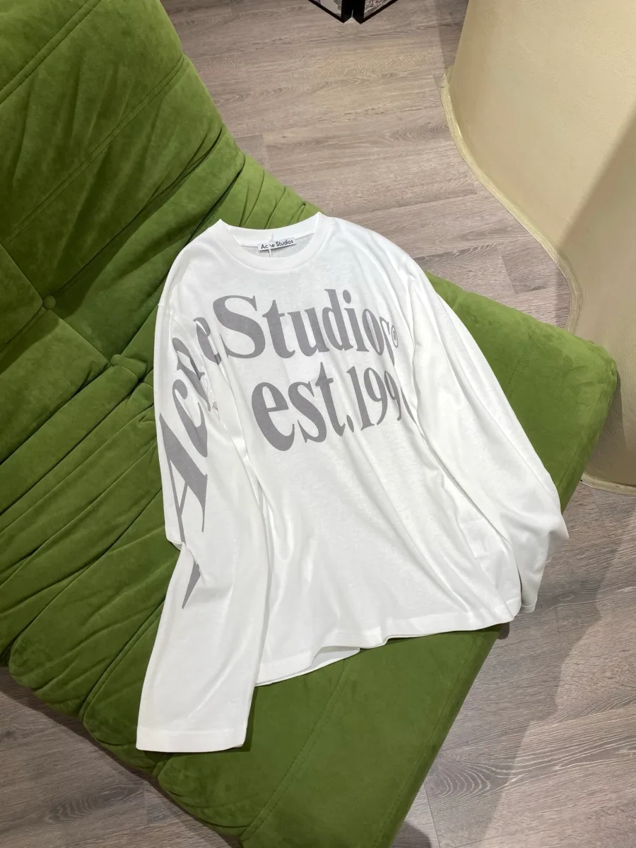 Белый свободный хлопковый лонгслив с принтом Studios est. 1996 на зелёном фоне