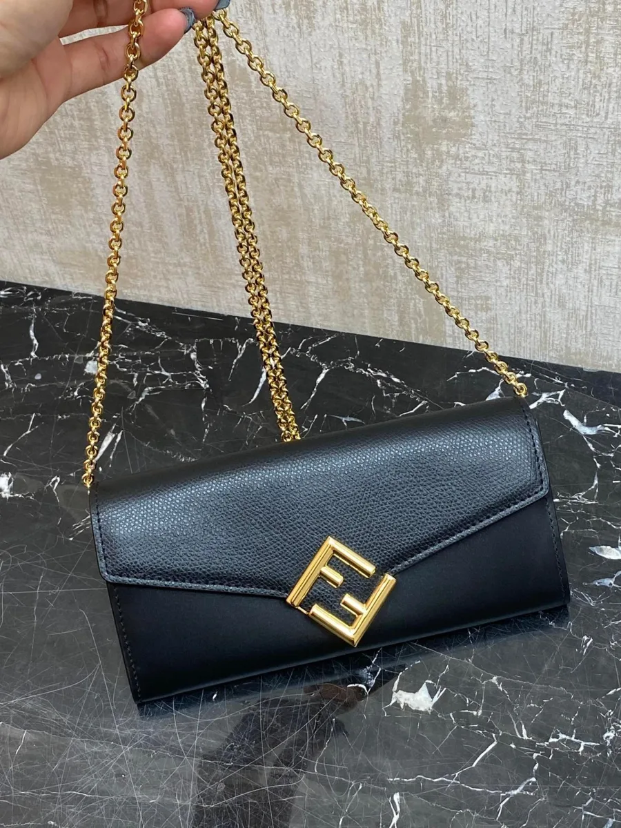 Чёрная сумка-кошелёк Fendi Diamonds на золотистой цепочке в руке, вид спереди