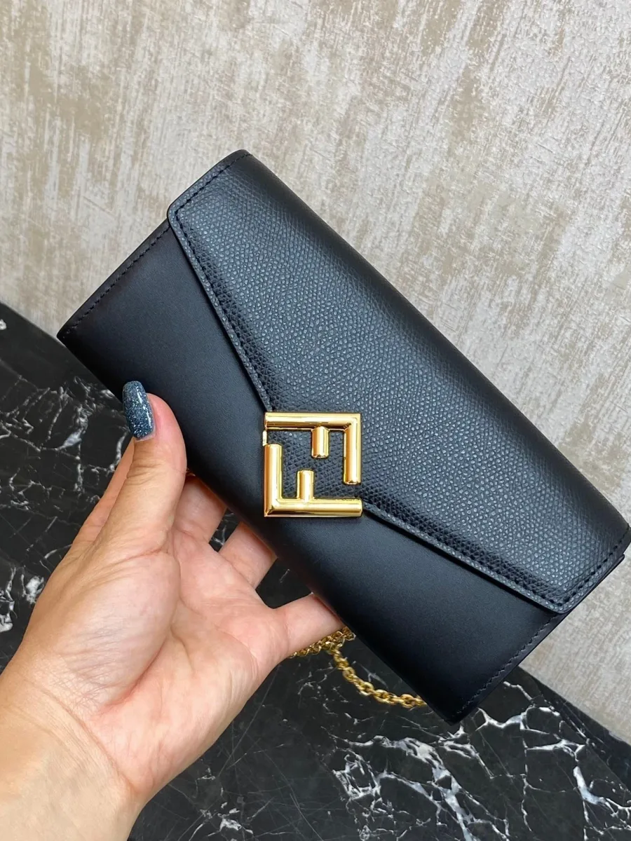 Чёрный кожаный кошелёк Fendi Diamonds с логотипом FF в руке на тёмном фоне