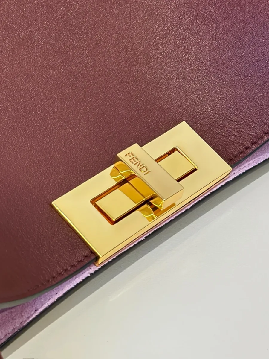 Крупный план золотистого поворотного замка с гравировкой Fendi на бордовой коже