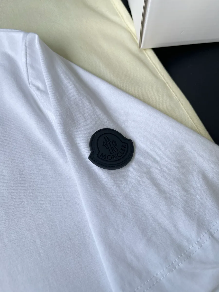 Рукав белой футболки с фирменной темной нашивкой-эмблемой крупным планом