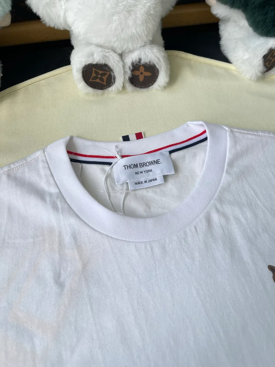Круглый вырез белой футболки с ярлыком Thom Browne и фирменной полосатой лентой