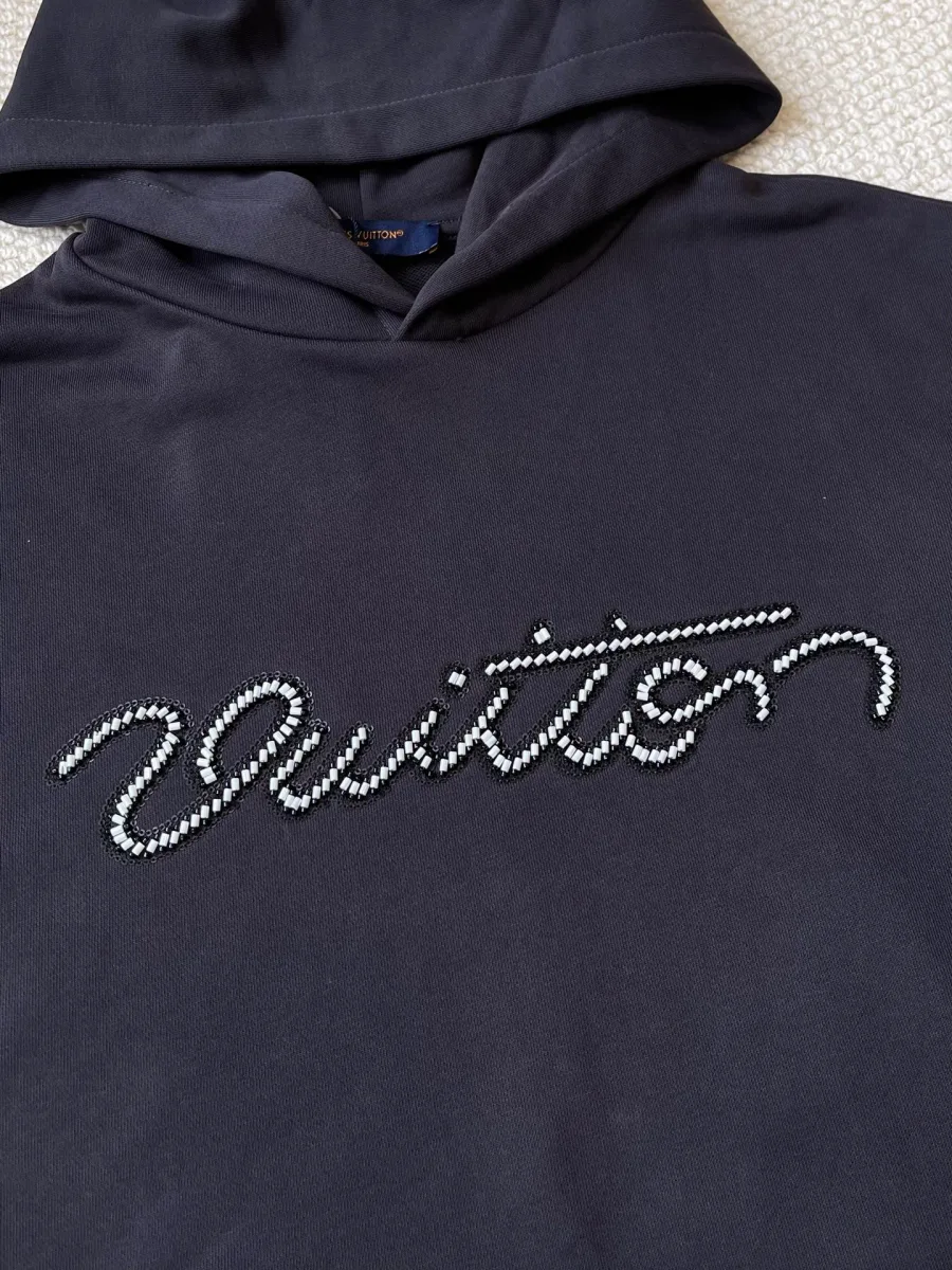 Выложенная бусинами курсивная надпись Vuitton на груди худи, макросъёмка