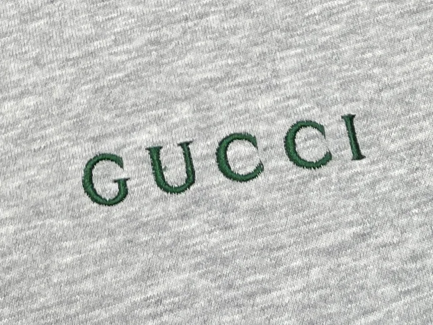 Вышитый тёмно-зелёный логотип Gucci крупным планом на сером трикотаже