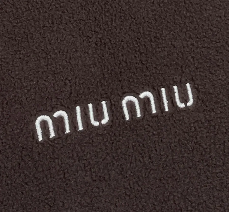 Контрастная белая вышивка логотипа Miu Miu на коричневом флисе крупным планом