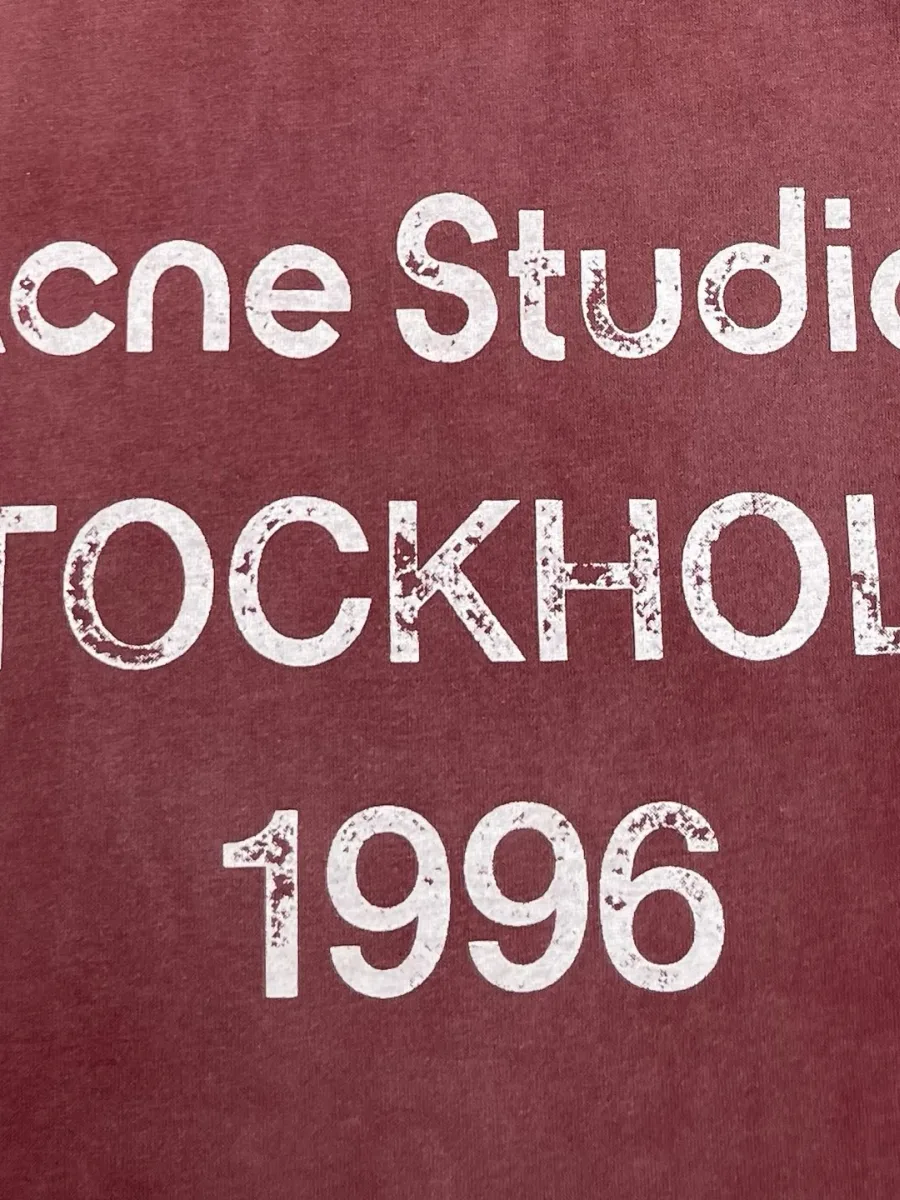 Крупный план белого принта Acne Studios Stockholm 1996 на груди