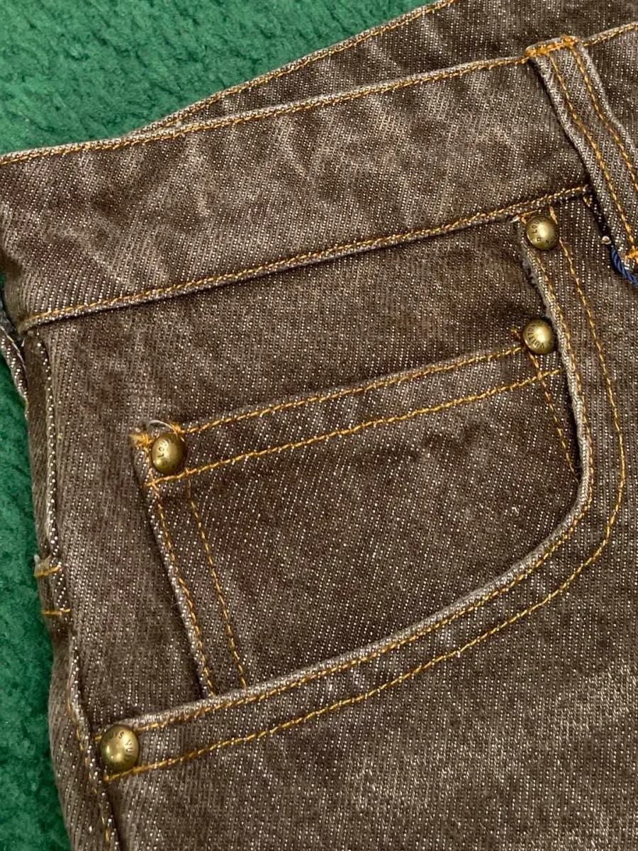 Передний прорезной карман коричневых джинсов с металлическими заклепками
