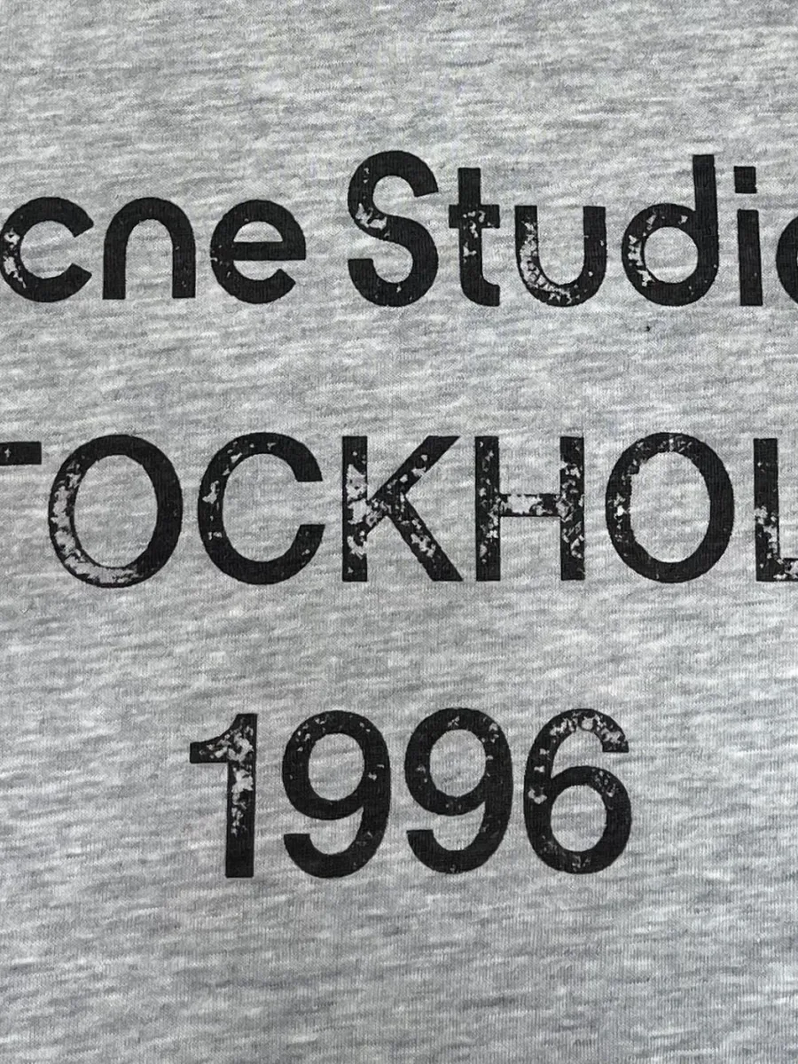 Крупный план текстового принта Acne Studios Stockholm 1996 на груди