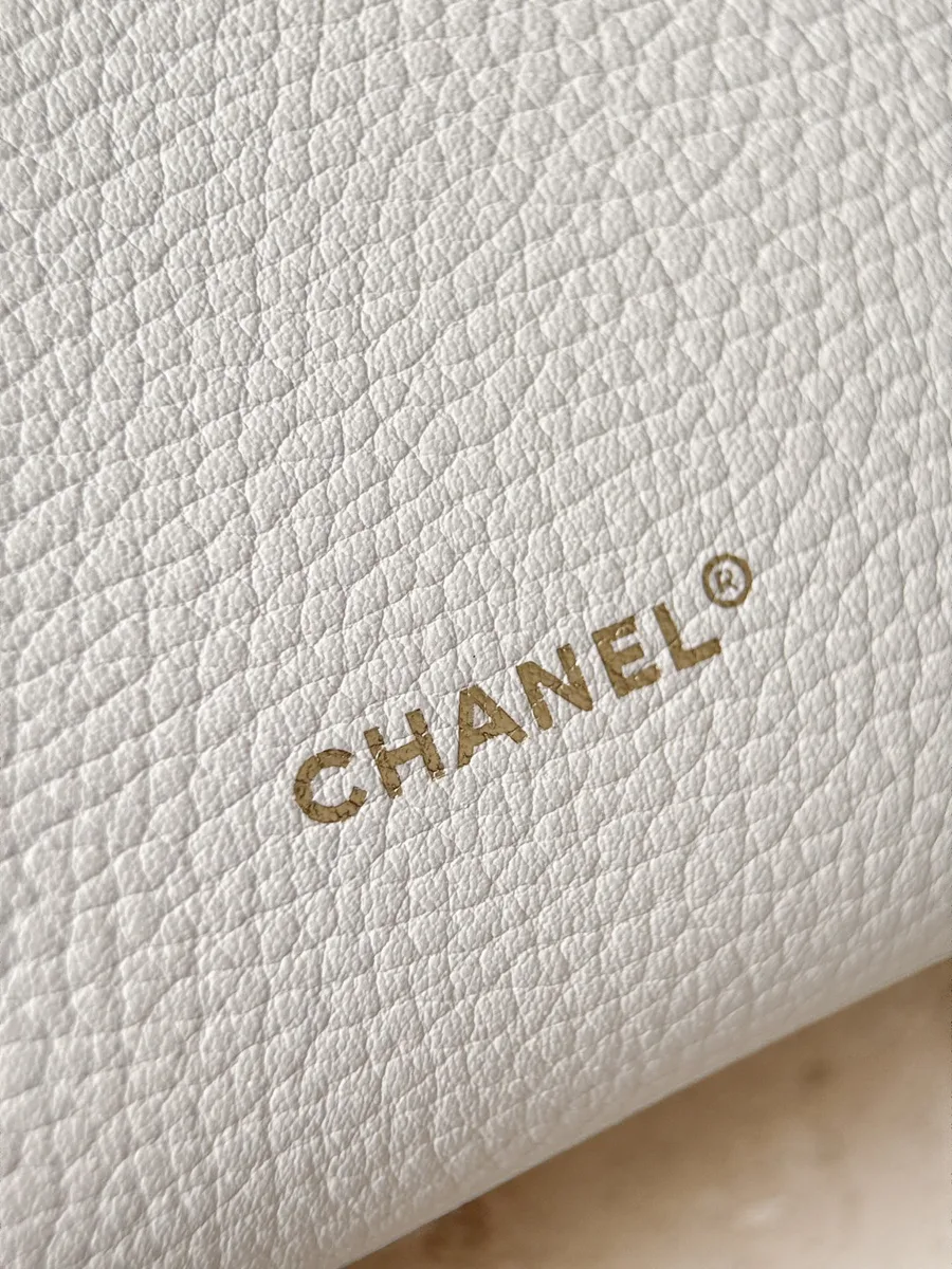 Крупный план тисненого золотистого логотипа Chanel на белой коже