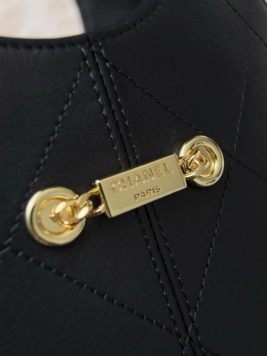 Крупный план золотистой пластины с гравировкой Chanel Paris на чёрной коже