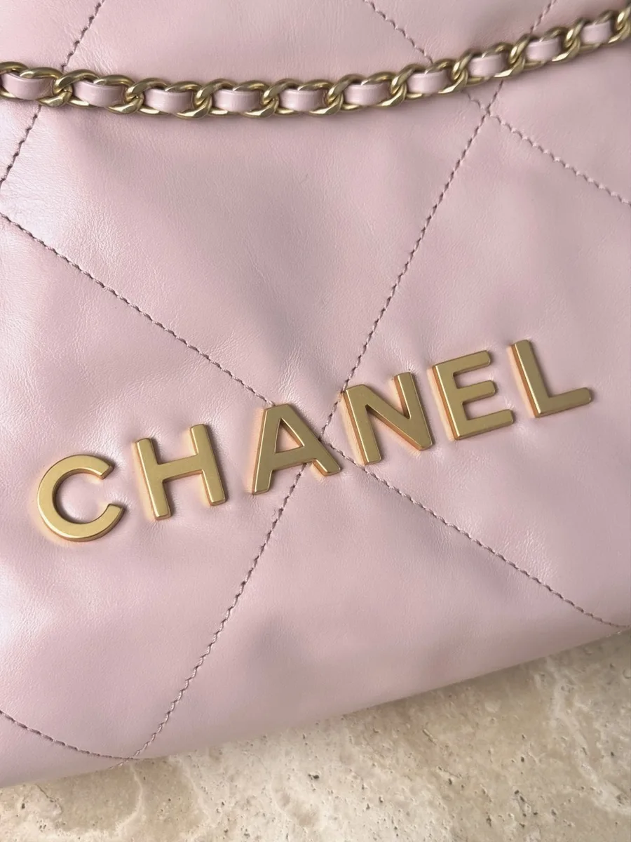 Крупный план золотистого металлического логотипа Chanel на розовой коже