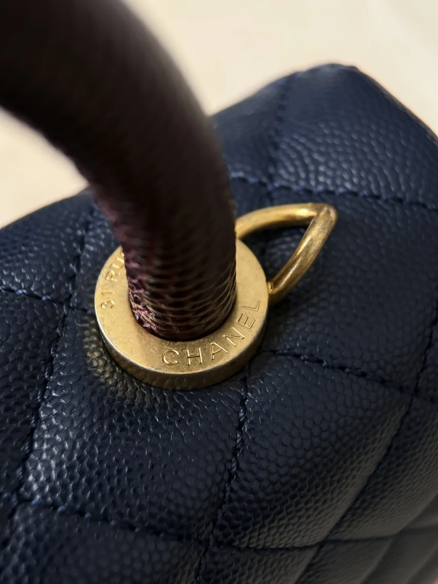 Крупный план крепления коричневой ручки с гравировкой Chanel на золотистом кольце