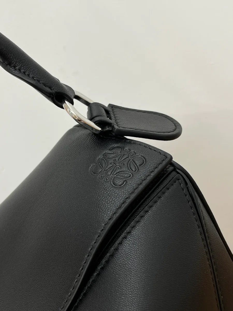 Тиснёный логотип Anagram на клапане чёрной сумки Loewe Puzzle, крупный план