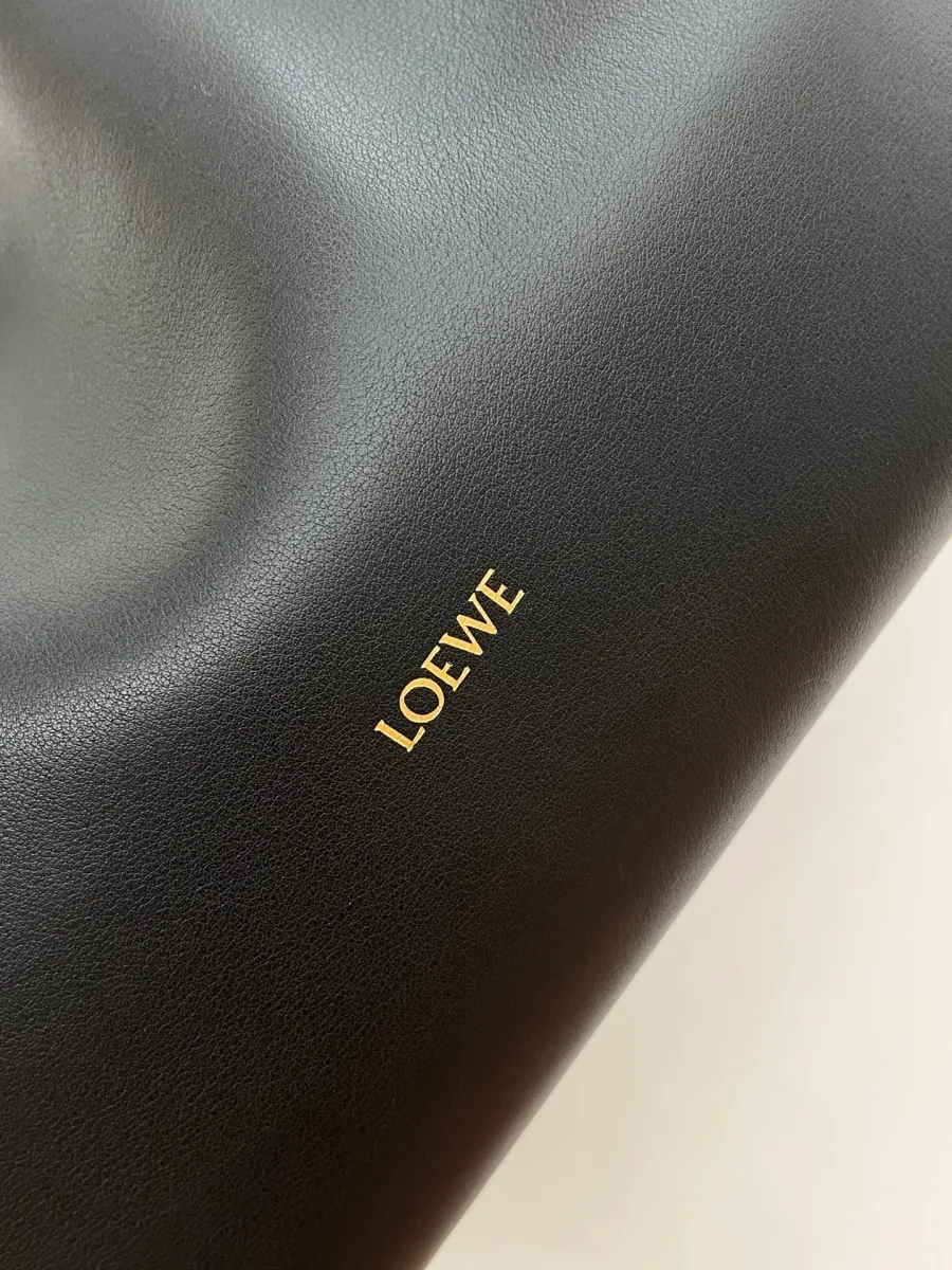 Золотистый принт с логотипом LOEWE на чёрной гладкой коже, крупный план