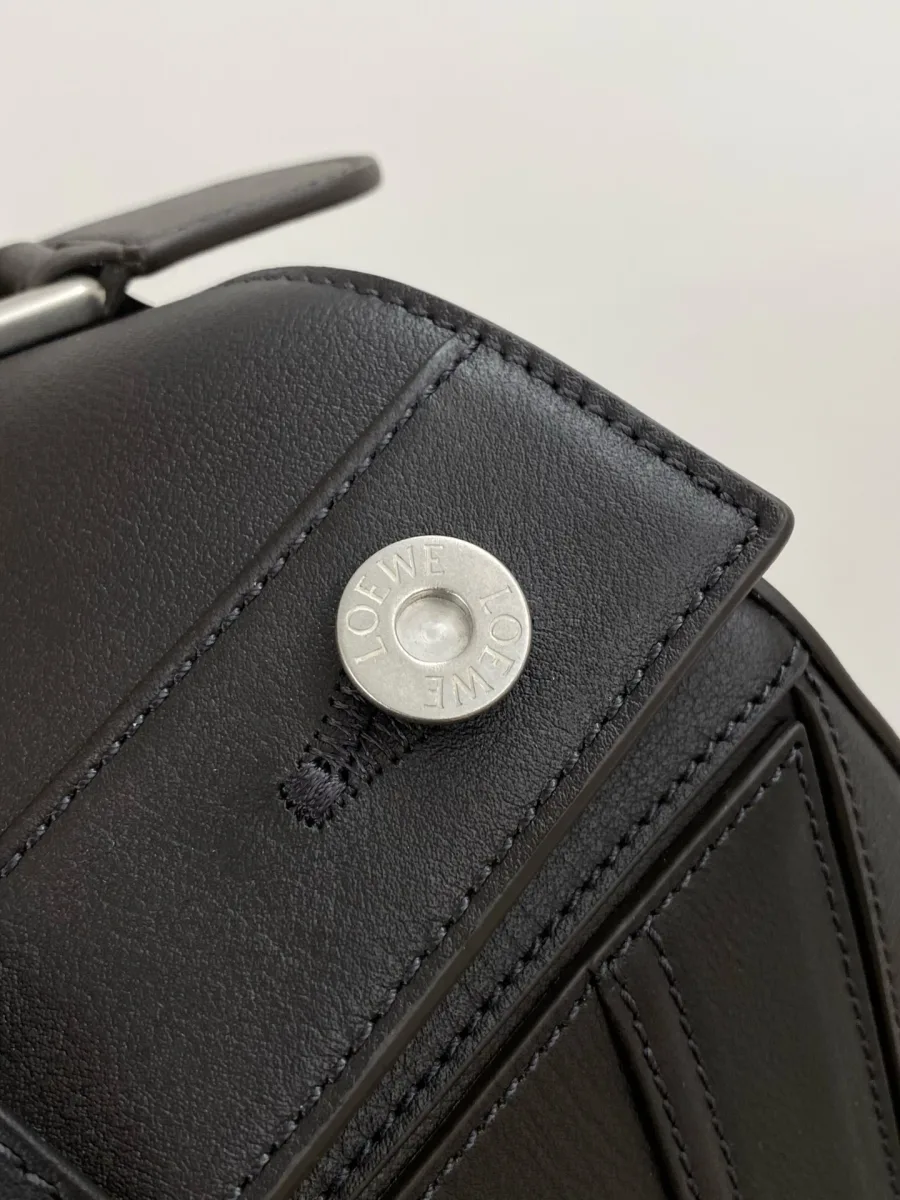 Крупный план металлической пуговицы с гравировкой Loewe на кожаном клапане сумки