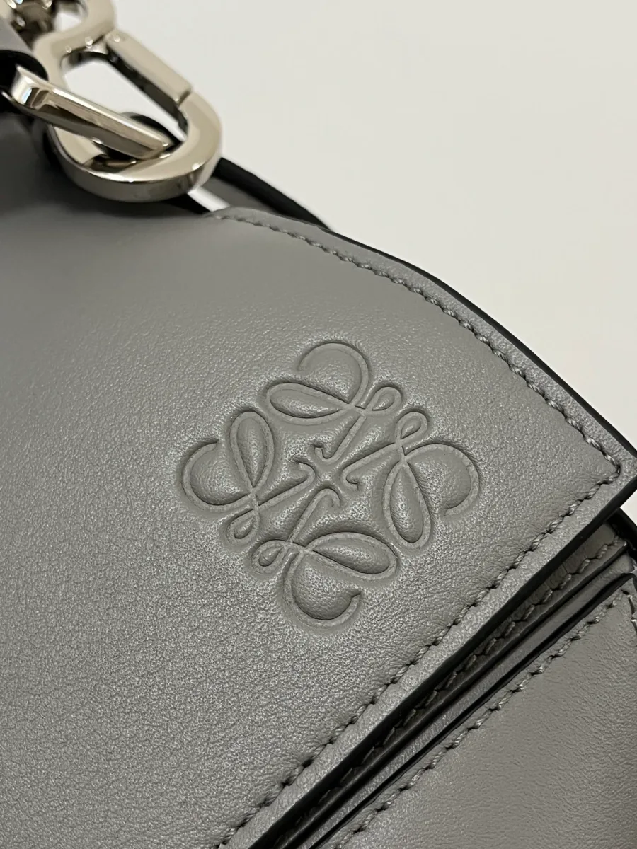 Тиснёный логотип-анаграмма Loewe на сером кожаном клапане сумки