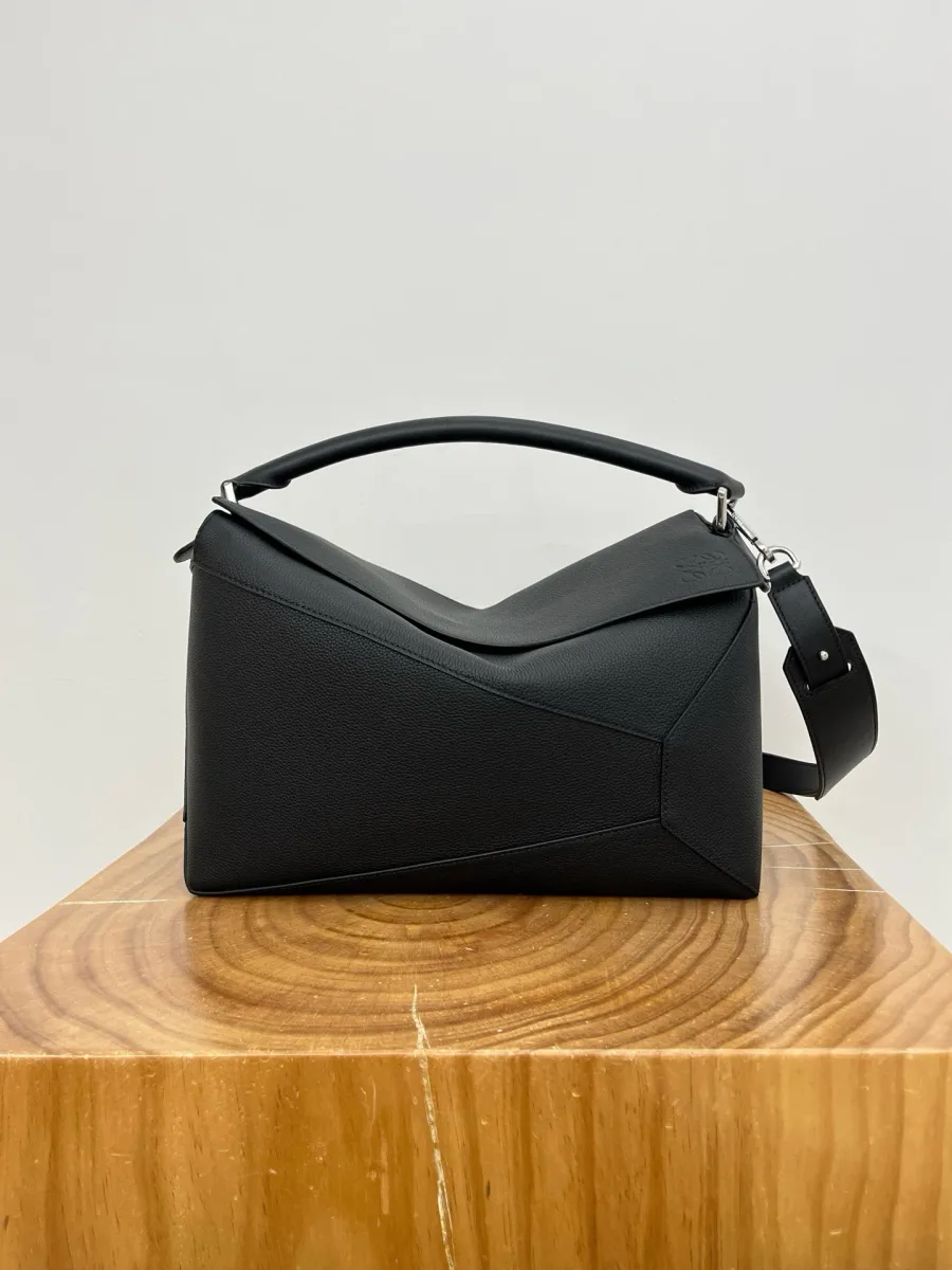 Чёрная кожаная сумка Loewe Puzzle 33 см, фронтальный ракурс на деревянной подставке