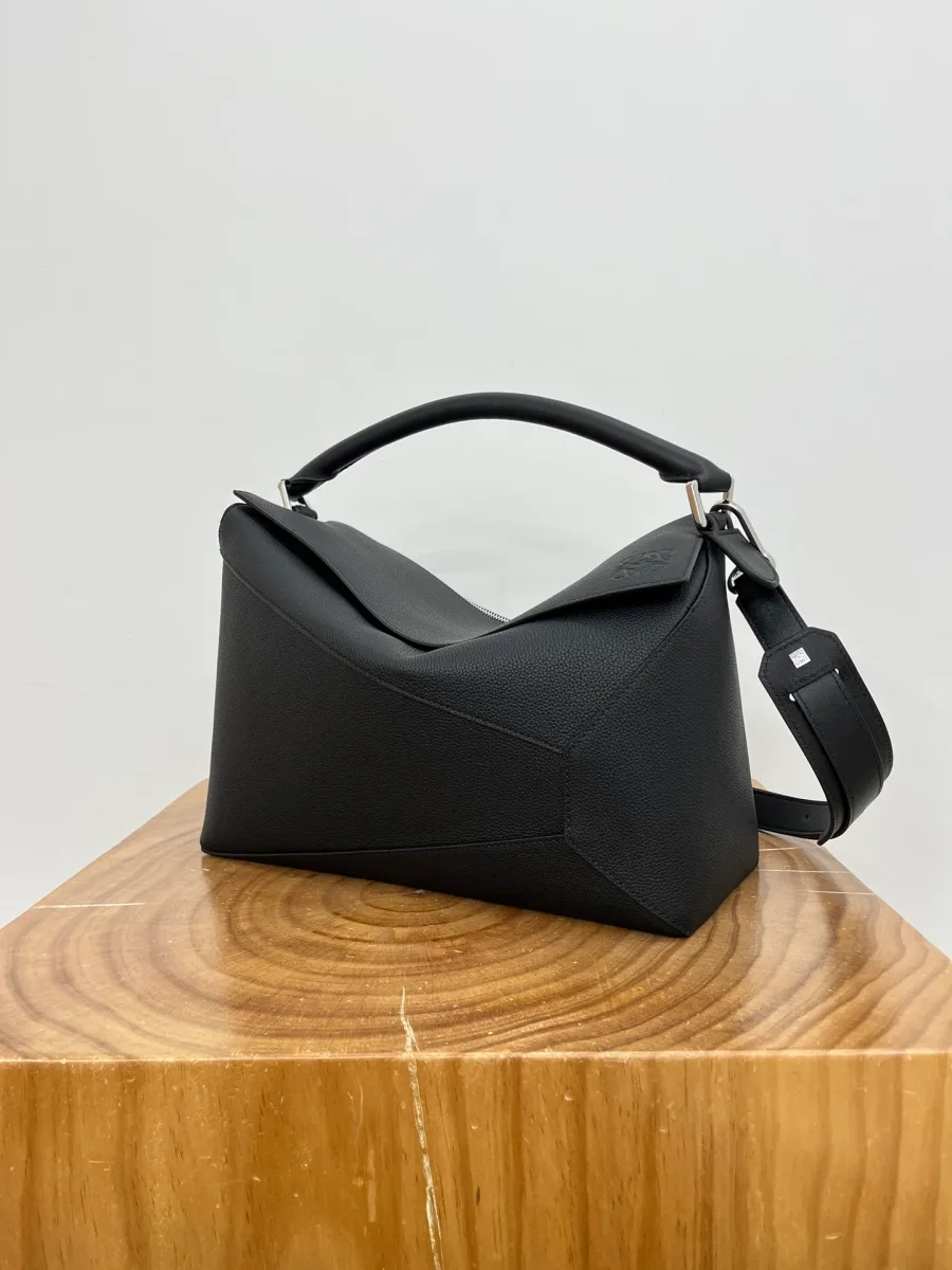 Сумка Loewe Puzzle из чёрной зернистой кожи, вид в три четверти с ручкой и ремнём