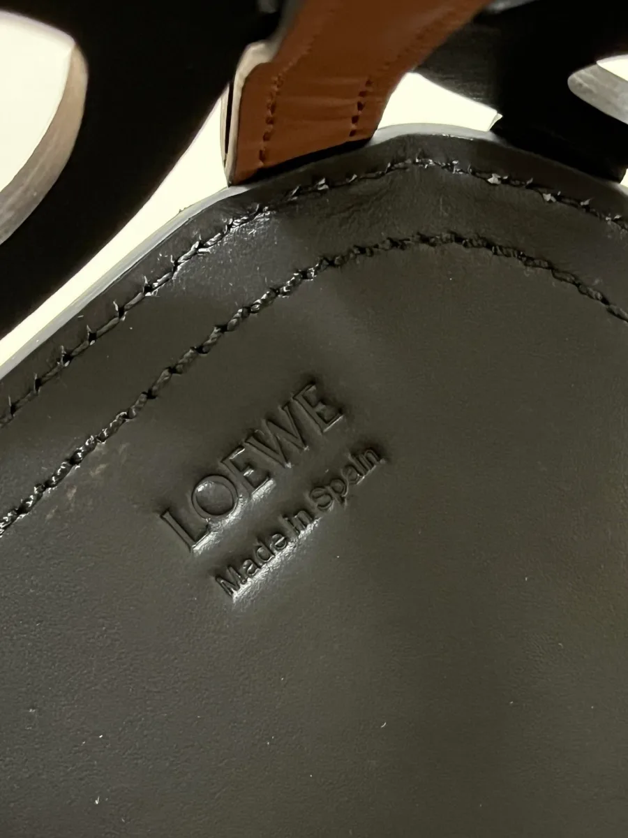 Тиснение бренда LOEWE Made in Spain на чёрной кожаной детали крупным планом