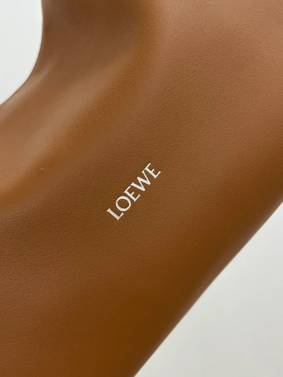 Серебристый логотип Loewe на гладкой коричневой коже сумки крупным планом
