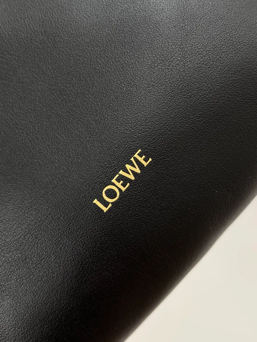 Золотистое тиснение логотипа Loewe на чёрной коже наппа, крупный план