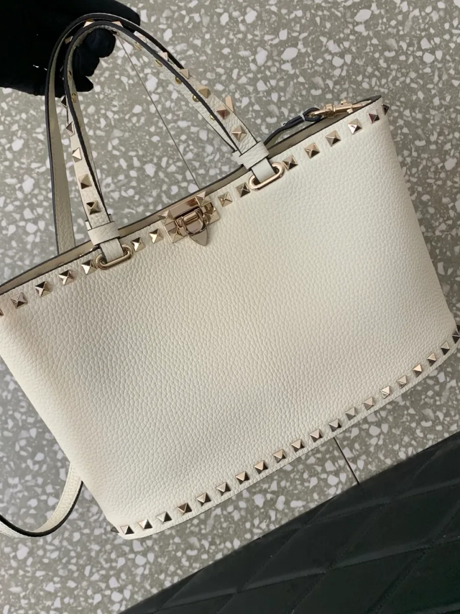 Белая сумка Valentino Rockstud в руке, демонстрация пропорций и силуэта