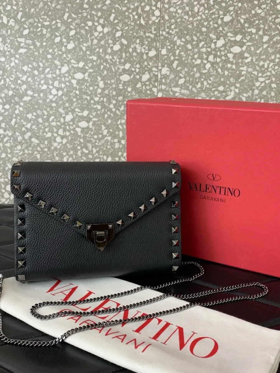 Чёрная сумка Valentino Rockstud рядом с фирменным пыльником и красной коробкой