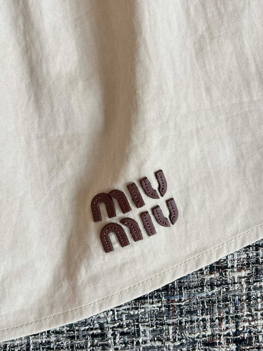 Вышитый контрастный логотип Miu Miu на подоле юбки крупным планом