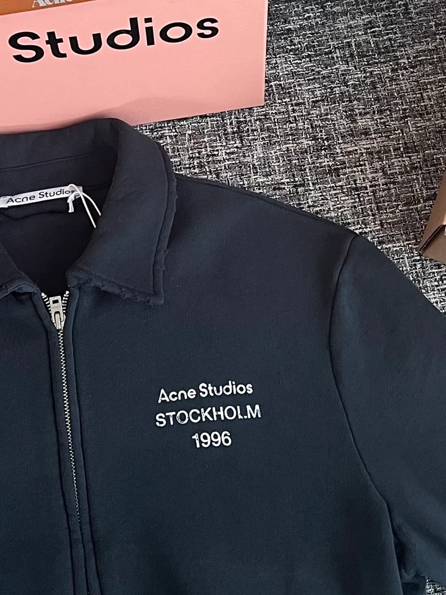 Крупный план контрастной вышивки Acne Studios Stockholm 1996 на груди