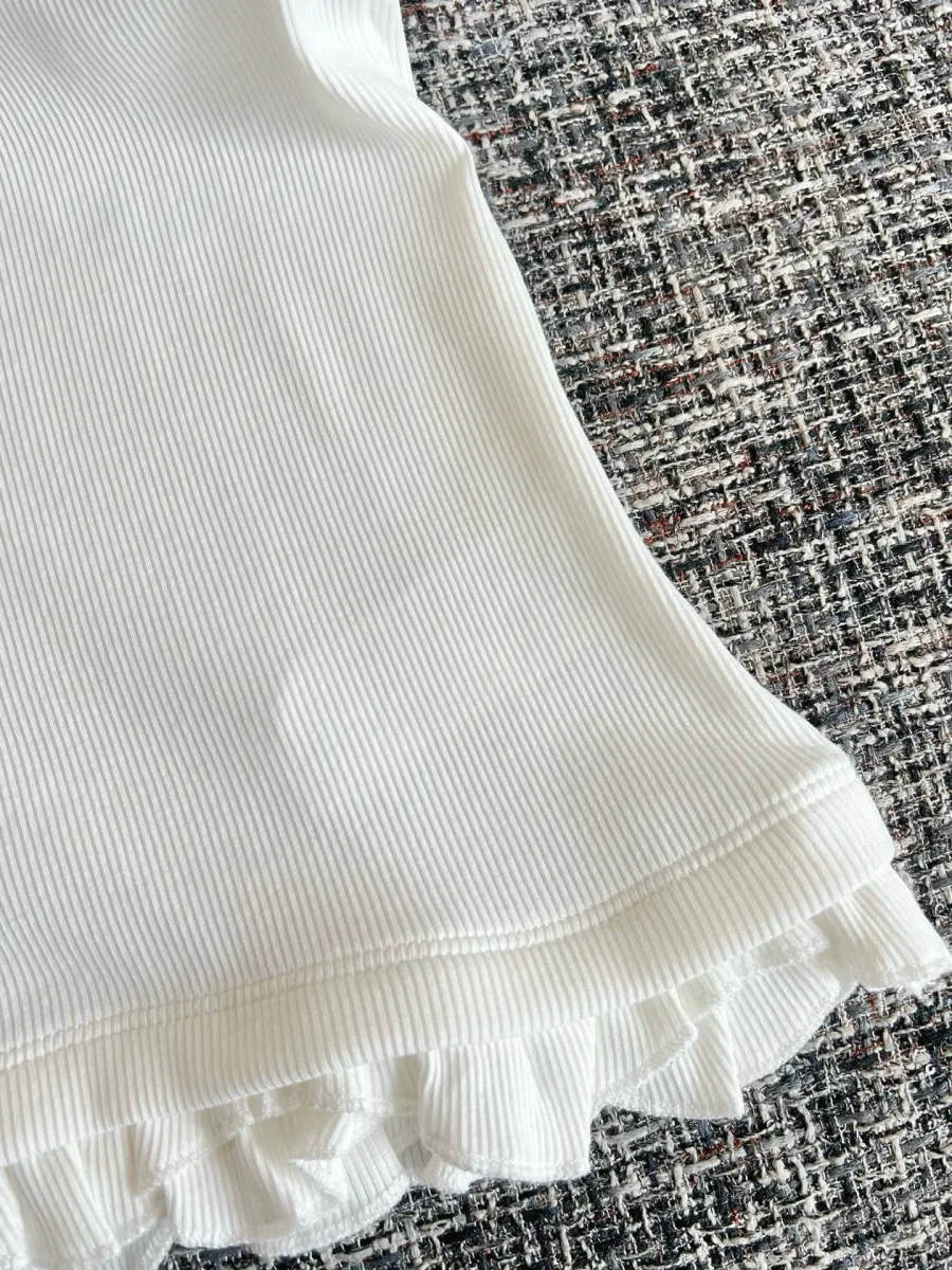 Нижний край белой майки с фактурной отделкой рюшами крупным планом