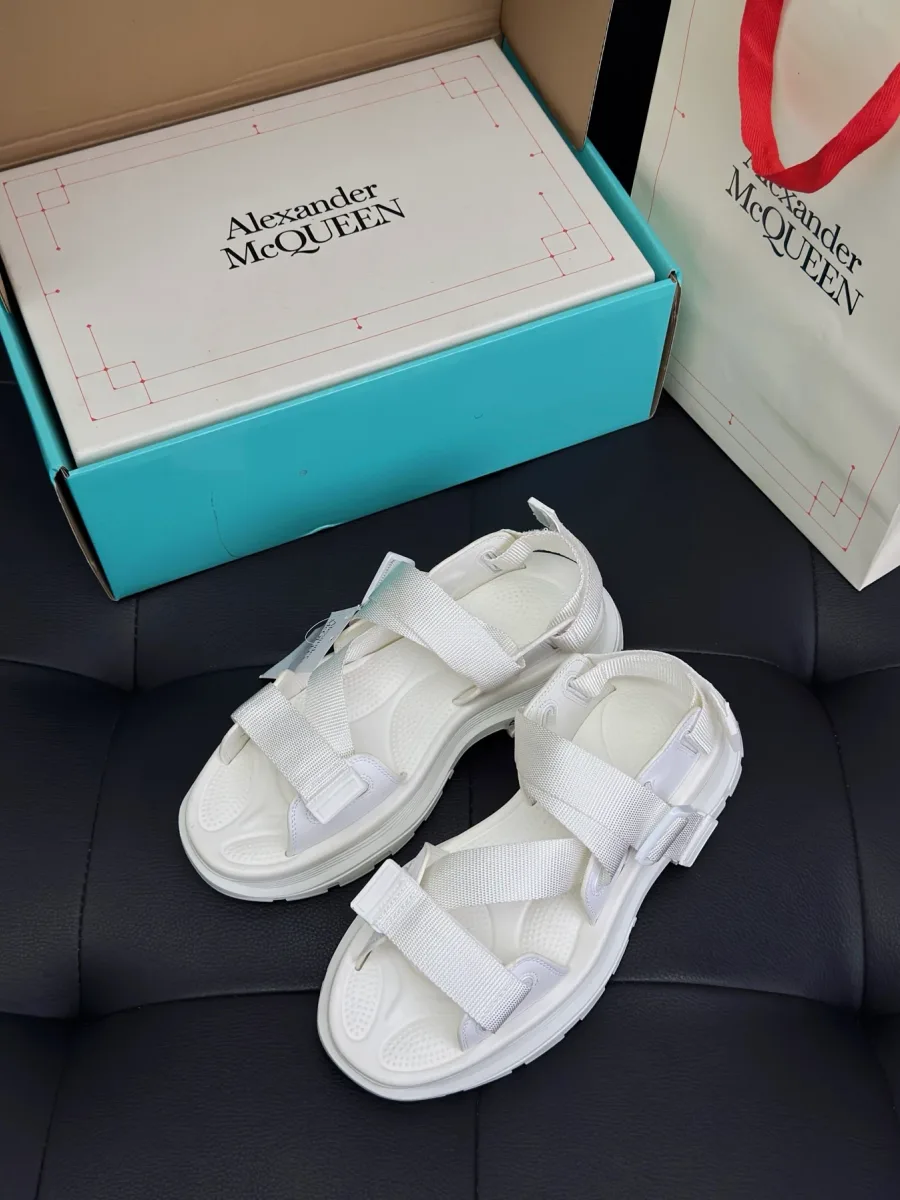 Белые сандалии Alexander McQueen Tread рядом с фирменной коробкой и пакетом