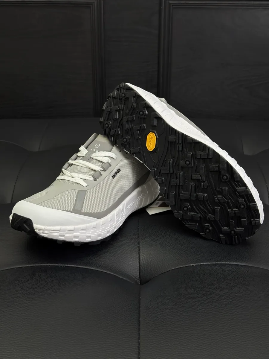 Кроссовок Norda 001 рядом с протектором подошвы Vibram с желтым логотипом