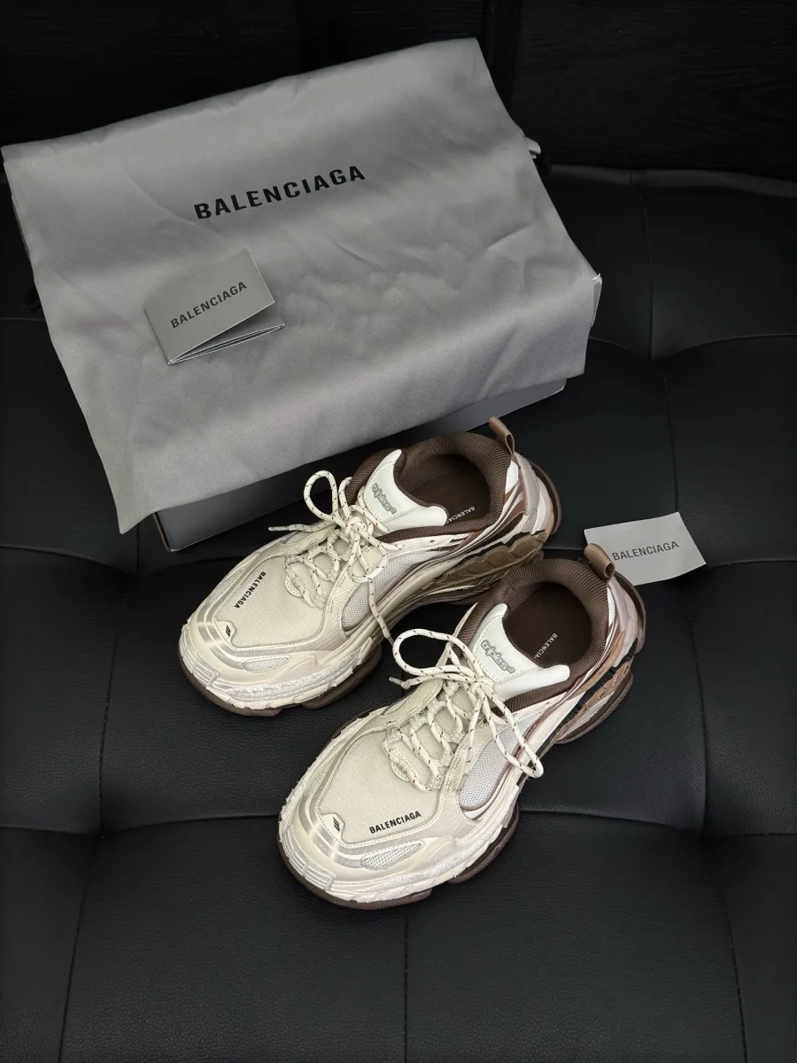 Кроссовки Balenciaga Triple S.2 бежевого цвета на чёрном фоне рядом с пыльником, вид сверху под углом