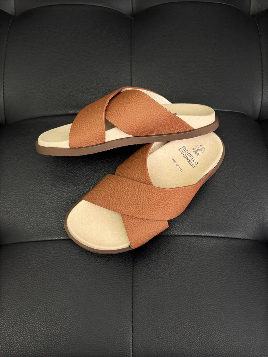 Пара коричневых кожаных шлёпанцев на черной поверхности, ракурс сбоку