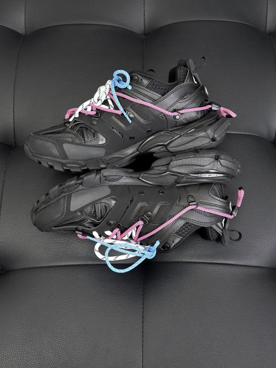 Пара чёрных кроссовок Balenciaga Track в профиль на тёмном кожаном фоне
